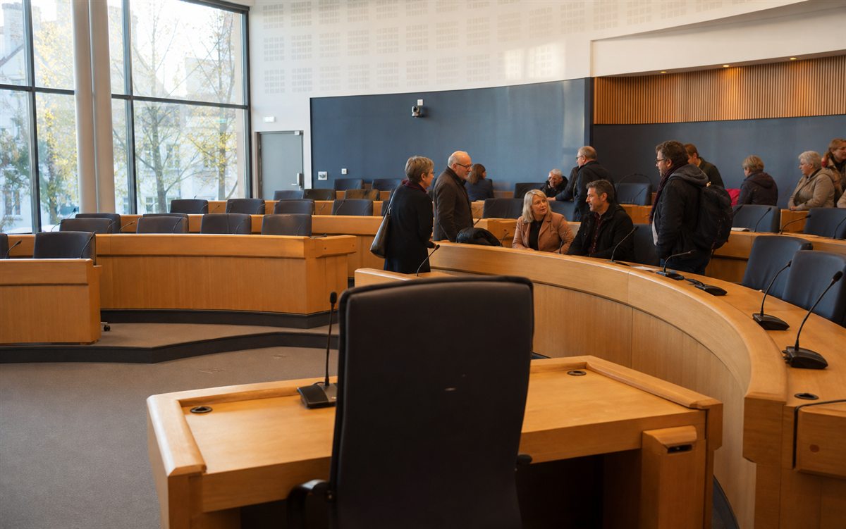 Salle de conseil municipal avec tables en bois et habitants prenant place